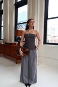 Woman in a strapless top and wide-leg pants standing in a room with large windows.